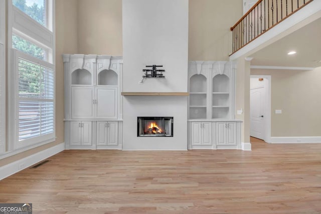 3451 Falls Branch Ct, Buford, GA 30519 - unfurnished living room with a towering ceiling, baseboards, light wood-style flooring, and a glass covered fireplace