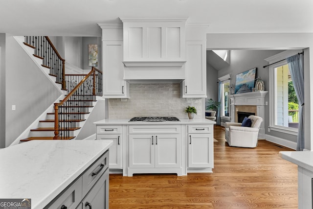 55 Jolie Ln, Sharpsburg, GA 30277 - kitchen featuring gas stovetop, decorative backsplash, a fireplace, light wood-style floors, and white cabinets