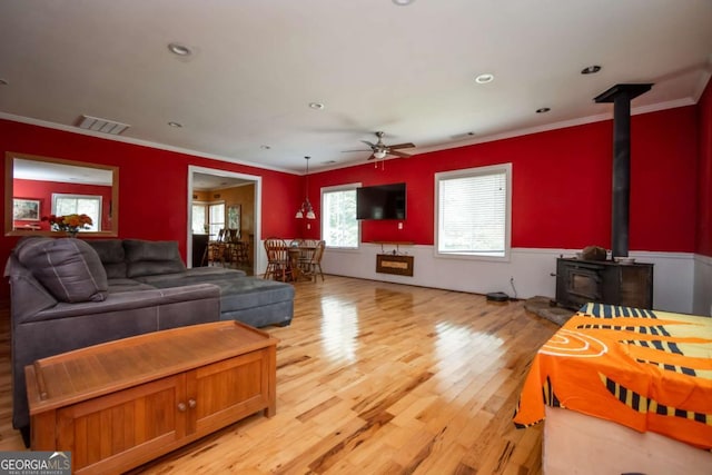 1079 Hardeman Farm Rd, Carnesville, GA 30521 - living area featuring light wood-style flooring, a wood stove, a ceiling fan, crown molding, and a wainscoted wall