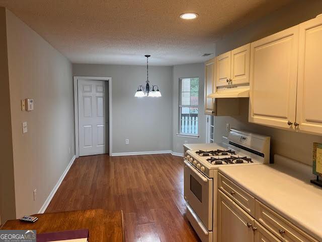 149 Titan Rd, Stockbridge, GA 30281 - kitchen with white gas range, under cabinet range hood, dark wood finished floors, a chandelier, and light countertops