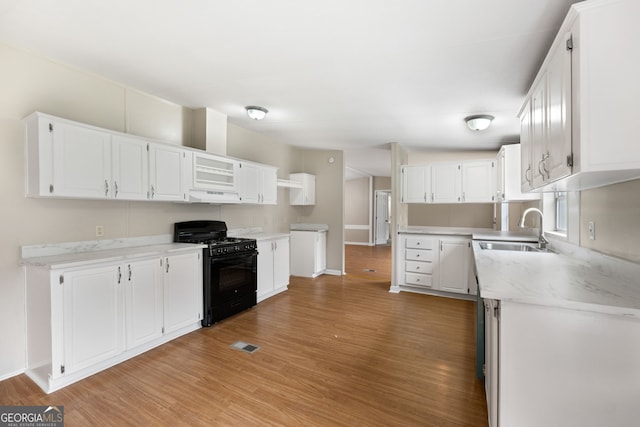 368 Hemlock Ln, Locust Grove, GA 30248 - kitchen with black gas range oven, a sink, under cabinet range hood, light wood-style floors, and white cabinetry