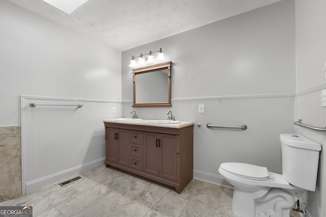 7972 Woods Ln, Jonesboro, GA 30236 - bathroom with a wainscoted wall, double vanity, toilet, baseboards, and a textured ceiling