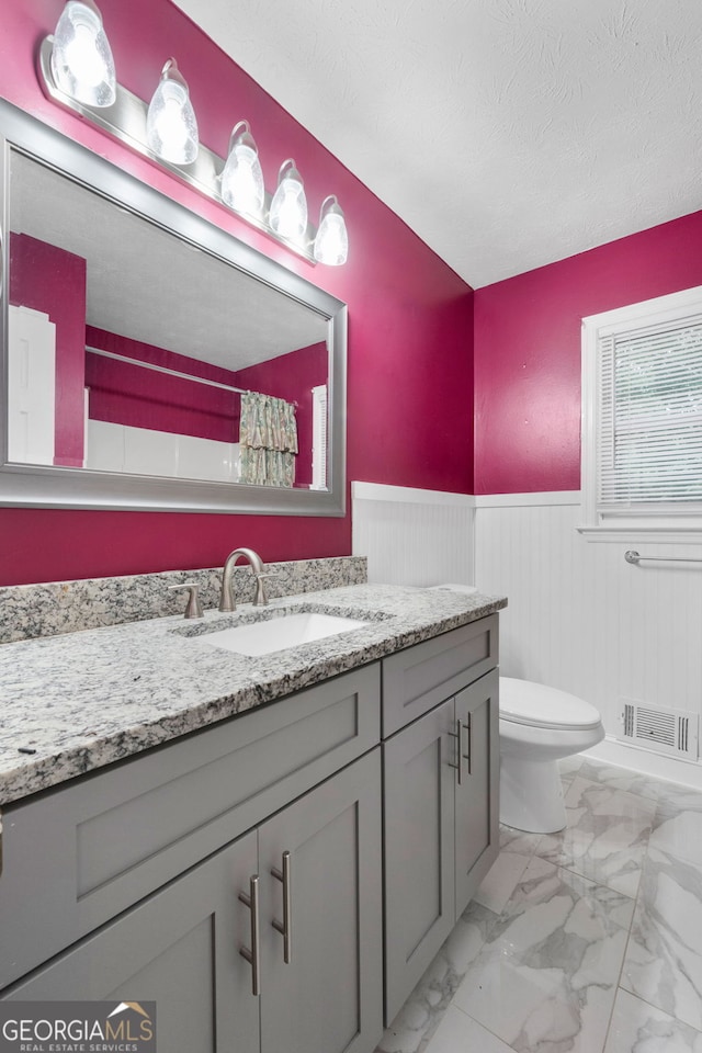 7972 Woods Ln, Jonesboro, GA 30236 - bathroom featuring a wainscoted wall, vanity, toilet, marble look tile flooring, and a textured ceiling