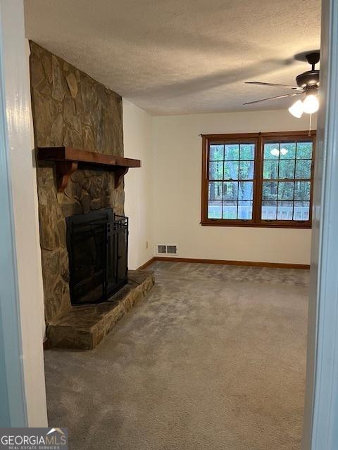 304 Tunis Rd, Mcdonough, GA 30253 - unfurnished living room featuring a textured ceiling, dark colored carpet, ceiling fan, and a stone fireplace