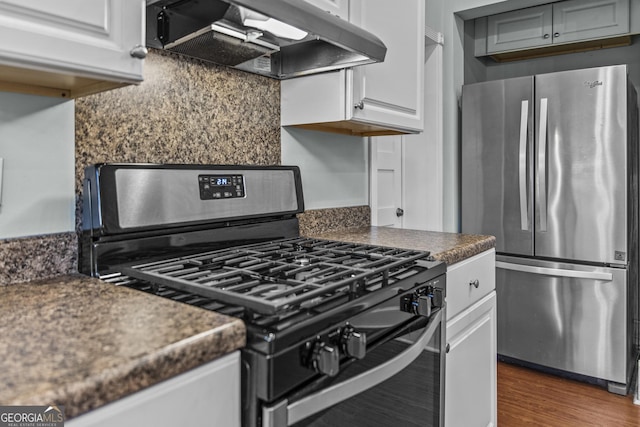 3119 Conyers St SE, Covington, GA 30014 - kitchen with appliances with stainless steel finishes, exhaust hood, dark countertops, dark wood finished floors, and white cabinets