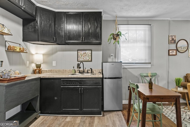 3119 Conyers St SE, Covington, GA 30014 - kitchen with freestanding refrigerator, a sink, dark cabinets, light wood finished floors, and a textured ceiling