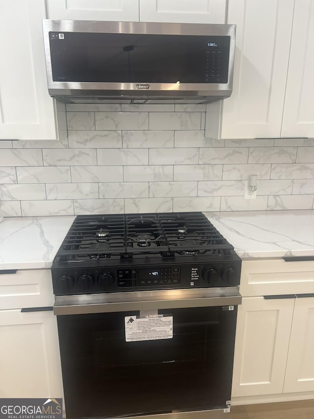 1340 Stoneleigh Way, Stone Mountain, GA 30088 - detailed view of black gas stove, stainless steel microwave, white cabinets, light stone counters, and backsplash