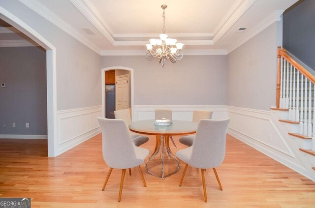 1570 Woodberry Run Dr, Snellville, GA 30078 - dining space featuring a chandelier, light wood finished floors, arched walkways, a raised ceiling, and a wainscoted wall