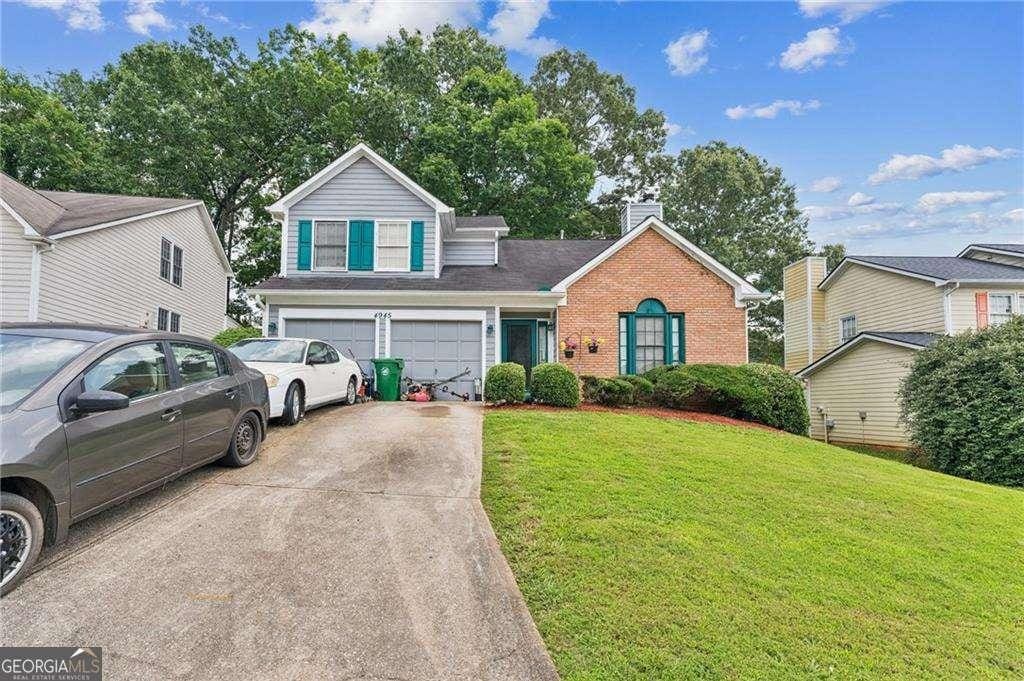 4945 Penscot Way, Stone Mountain, GA 30088 - traditional-style home with concrete driveway, brick siding, an attached garage, a front lawn, and a chimney