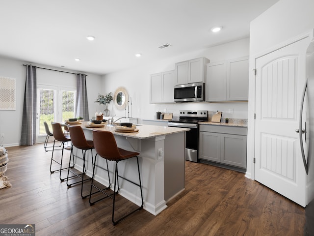 8215 Coldstream Dr, Fairburn, GA 30213 - kitchen with stainless steel appliances, gray cabinets, a kitchen island with sink, a kitchen bar, and light stone counters