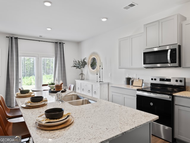 8215 Coldstream Dr, Fairburn, GA 30213 - kitchen featuring stainless steel microwave, electric range oven, a sink, light stone countertops, and an island with sink