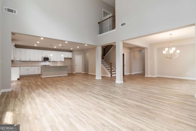 4000 Red Canoe Bnd, Lilburn, GA 30047 - unfurnished living room featuring a chandelier, stairway, light wood-style floors, a towering ceiling, and baseboards