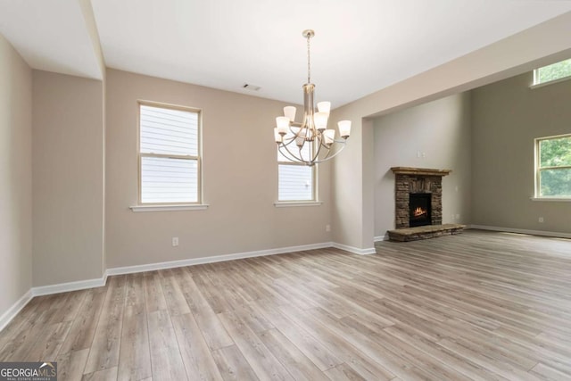 4000 Red Canoe Bnd, Lilburn, GA 30047 - unfurnished living room featuring a chandelier, light wood-style flooring, a stone fireplace, and baseboards