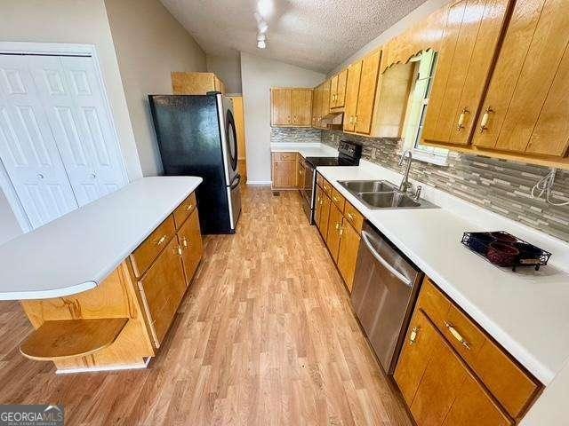 198 Swift Creek Rd, Cordele, GA 31015 - kitchen featuring appliances with stainless steel finishes, light wood finished floors, brown cabinetry, backsplash, and vaulted ceiling