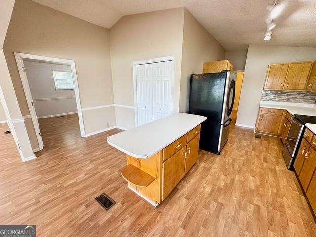 198 Swift Creek Rd, Cordele, GA 31015 - kitchen featuring freestanding refrigerator, brown cabinetry, light wood finished floors, light countertops, and vaulted ceiling