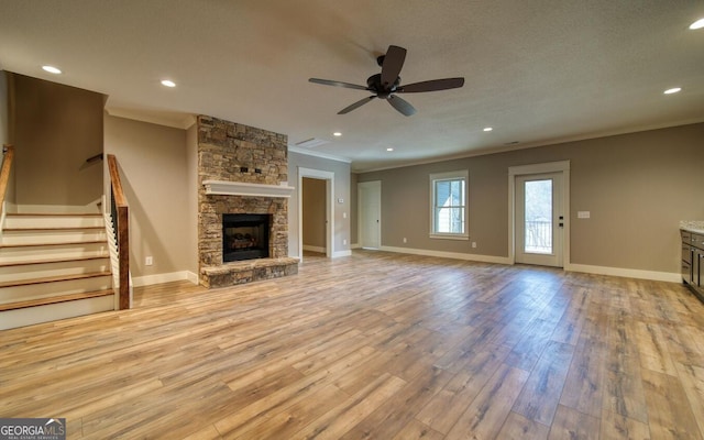 2628 Rolling River Dr, Hiawassee, GA 30546 - unfurnished living room with crown molding, light wood-style flooring, ceiling fan, a stone fireplace, and stairs