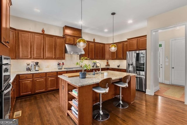 5830 Caveat Ct, Suwanee, GA 30024 - kitchen featuring appliances with stainless steel finishes, under cabinet range hood, brown cabinets, dark wood-type flooring, and recessed lighting