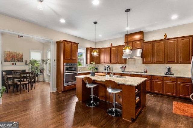 5830 Caveat Ct, Suwanee, GA 30024 - kitchen featuring appliances with stainless steel finishes, exhaust hood, brown cabinets, dark wood-style floors, and tasteful backsplash