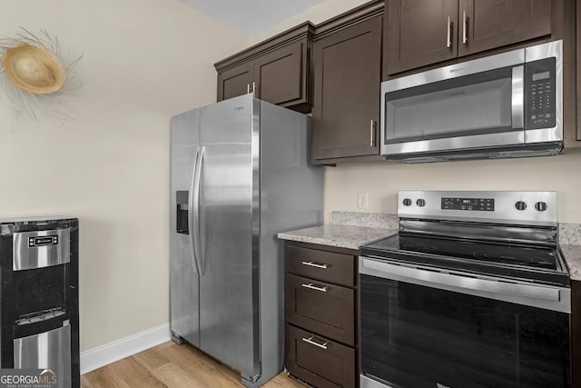 935 Abode Ave, Fort Stewart, GA 31313 - kitchen with stainless steel appliances, light wood-style flooring, dark brown cabinetry, light stone counters, and baseboards