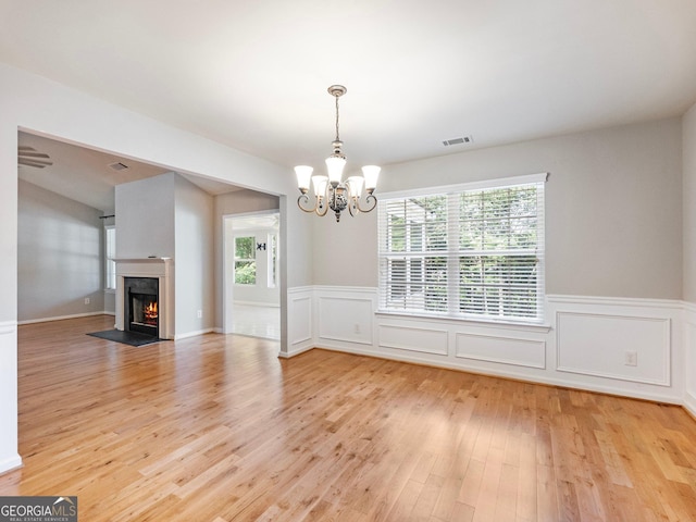 6439 Mossy Boulder Dr, Flowery Branch, GA 30542 - unfurnished living room featuring light wood-style flooring, a chandelier, a wainscoted wall, a fireplace with flush hearth, and a decorative wall
