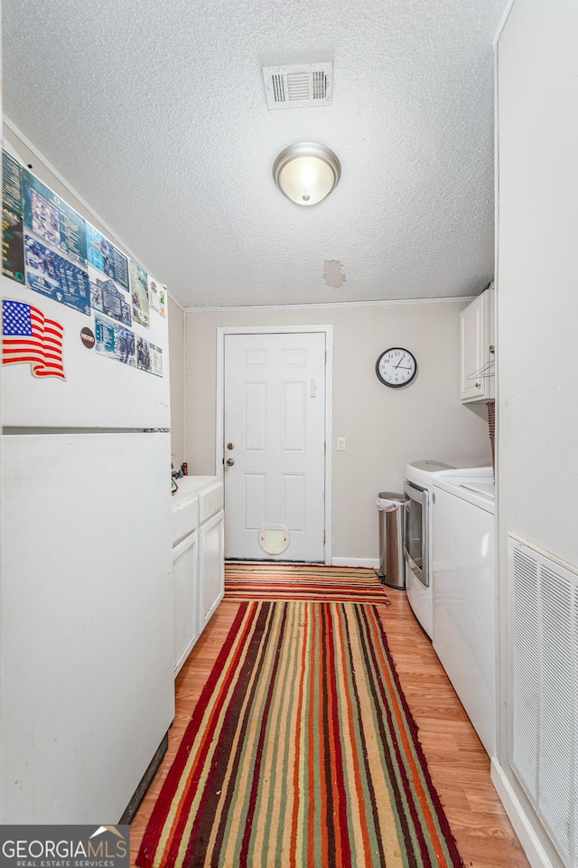 6162 Ayrin Brooke Ln, Blackshear, GA 31516 - laundry room featuring washer and dryer, cabinet space, a textured ceiling, light wood-type flooring, and baseboards