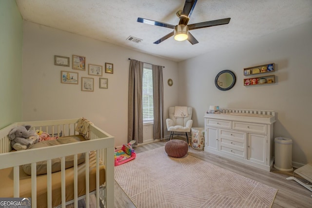 527 Malcom Rd, Covington, GA 30014 - bedroom with light wood-style flooring, a crib, a textured ceiling, ceiling fan, and baseboards
