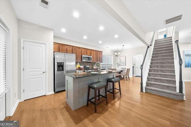 3607 Archgate Ct, Alpharetta, GA 30004 - kitchen featuring appliances with stainless steel finishes, an island with sink, dark countertops, a breakfast bar, and brown cabinets