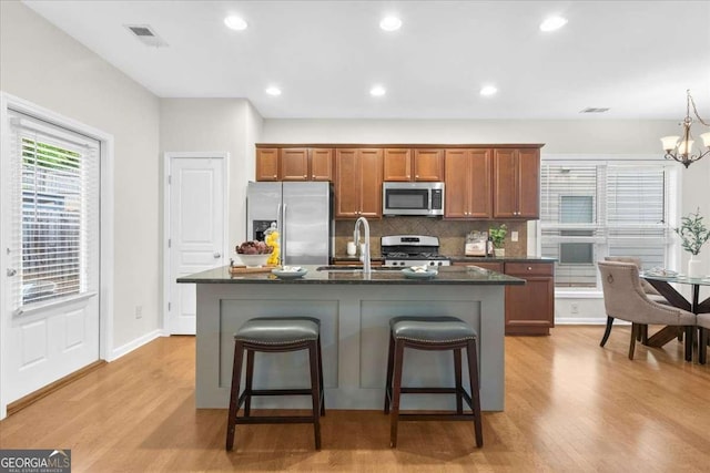 3607 Archgate Ct, Alpharetta, GA 30004 - kitchen featuring stainless steel appliances, brown cabinetry, backsplash, light wood-type flooring, and a center island with sink