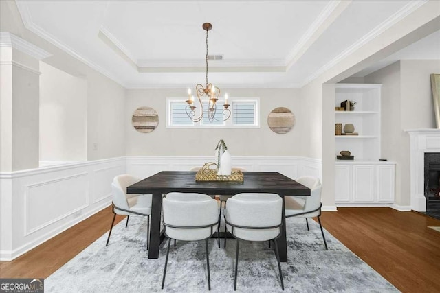 3607 Archgate Ct, Alpharetta, GA 30004 - dining space featuring wood finished floors, a chandelier, a tray ceiling, a glass covered fireplace, and crown molding