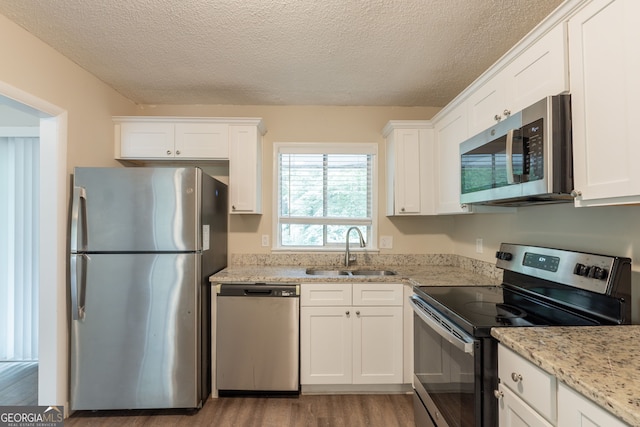 4669 Birch Ridge Trl, Stone Mountain, GA 30083 - kitchen featuring stainless steel appliances, wood finished floors, white cabinetry, a textured ceiling, and light stone counters