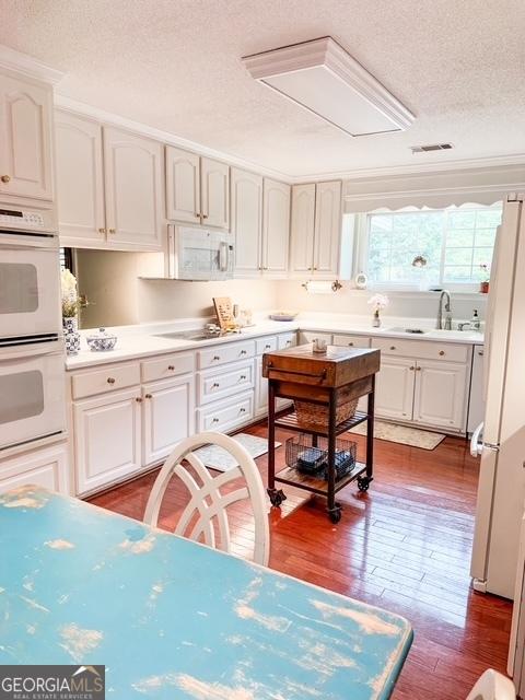 507 S College St, Metter, GA 30439 - kitchen with a sink, white appliances, a textured ceiling, white cabinets, and wood finished floors