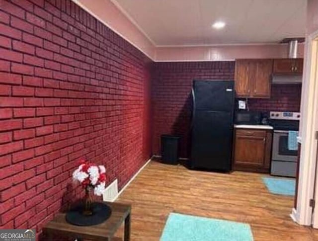 4157 Cedar Valley Ln, Conley, GA 30288 - kitchen with freestanding refrigerator, electric range, under cabinet range hood, brick wall, and light wood-style flooring