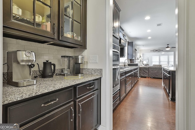 819 Firefly Ct, Griffin, GA 30223 - kitchen with dark brown cabinetry, wood finished floors, backsplash, glass insert cabinets, and light stone countertops