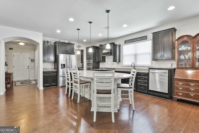 819 Firefly Ct, Griffin, GA 30223 - kitchen with appliances with stainless steel finishes, arched walkways, decorative backsplash, a breakfast bar area, and light stone countertops