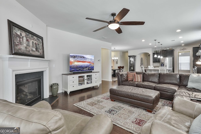 819 Firefly Ct, Griffin, GA 30223 - living room featuring a ceiling fan, a chandelier, arched walkways, dark wood finished floors, and a glass covered fireplace