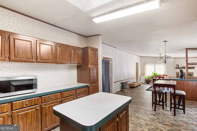 294 Birch Rd, Franklin, GA 30217 - kitchen featuring stainless steel microwave, dark stone finish floors, brown cabinetry, a kitchen island, and a chandelier