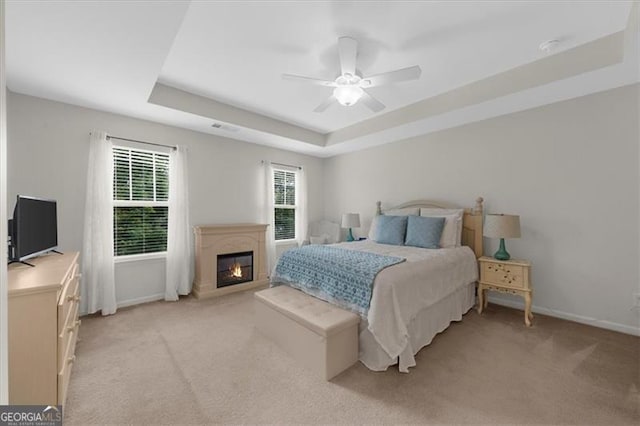 397 Cypher Dr, Suwanee, GA 30024 - bedroom with a tray ceiling, light carpet, a ceiling fan, and a glass covered fireplace
