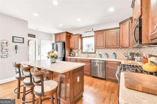 125 Shamus Way, Jefferson, GA 30549 - kitchen featuring stainless steel appliances, light wood-style flooring, a kitchen island, backsplash, and a kitchen breakfast bar