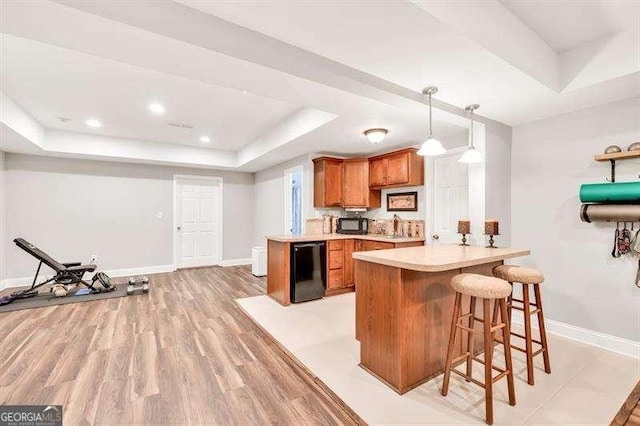 125 Shamus Way, Jefferson, GA 30549 - kitchen featuring a tray ceiling, brown cabinetry, light wood-type flooring, a peninsula, and a kitchen bar