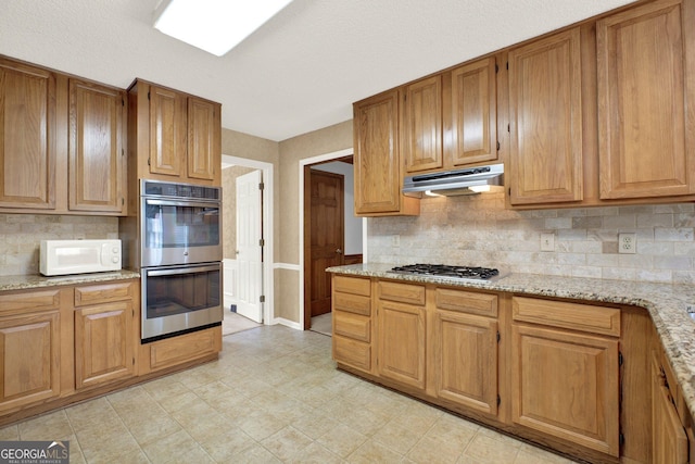 4313 Deep Springs Ct NW, Kennesaw, GA 30144 - kitchen with under cabinet range hood, appliances with stainless steel finishes, decorative backsplash, and light stone countertops