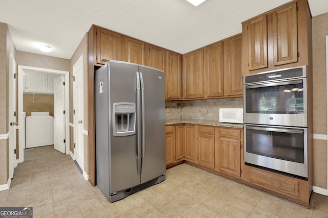 4313 Deep Springs Ct NW, Kennesaw, GA 30144 - kitchen with appliances with stainless steel finishes, washer and clothes dryer, light stone countertops, brown cabinets, and a textured ceiling