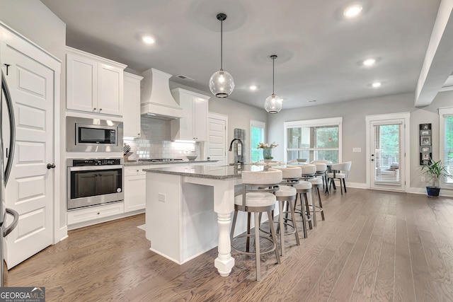 29 Peppertree Dr, Newnan, GA 30265 - kitchen with stainless steel appliances, custom range hood, recessed lighting, an island with sink, and light wood-style floors