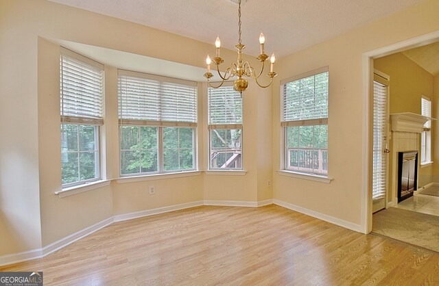 4135 Coursey Lake Rd, Douglasville, GA 30135 - unfurnished dining area featuring light wood-type flooring, a chandelier, plenty of natural light, a tiled fireplace, and a textured ceiling
