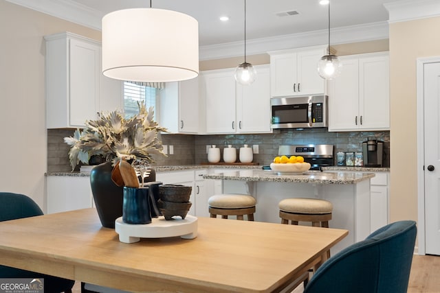 155 Roxeywood Way, Winder, GA 30680 - kitchen with stainless steel appliances, ornamental molding, a center island, white cabinetry, and decorative light fixtures