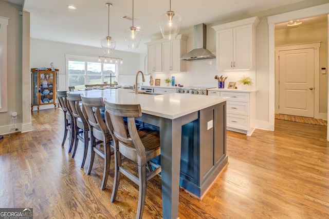 3076 E Lake Rd, Mcdonough, GA 30252 - kitchen with wall chimney exhaust hood, a kitchen island with sink, light wood-style floors, and white cabinets