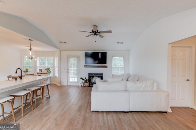 1406 Marshview Ct, Hoschton, GA 30548 - living area featuring lofted ceiling, light wood finished floors, a ceiling fan, a glass covered fireplace, and a chandelier