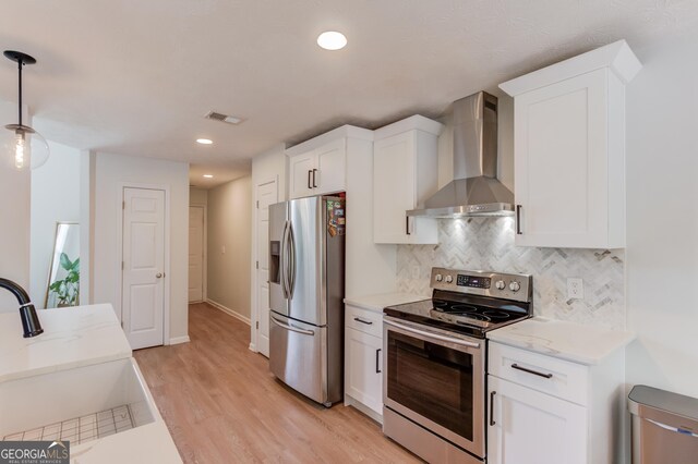 1406 Marshview Ct, Hoschton, GA 30548 - kitchen with appliances with stainless steel finishes, wall chimney exhaust hood, light wood-style floors, white cabinetry, and decorative backsplash
