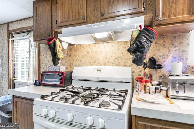 912 Druid St, Dublin, GA 31021 - kitchen with white gas range, wallpapered walls, under cabinet range hood, light countertops, and brown cabinets