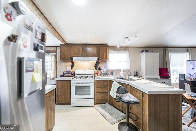 912 Druid St, Dublin, GA 31021 - kitchen featuring freestanding refrigerator, white range with gas cooktop, under cabinet range hood, a peninsula, and light countertops