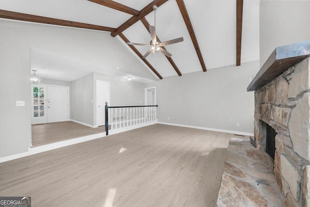 2945 Thompson Mill Rd, Gainesville, GA 30506 - unfurnished living room featuring a stone fireplace, a ceiling fan, beamed ceiling, wood finished floors, and high vaulted ceiling